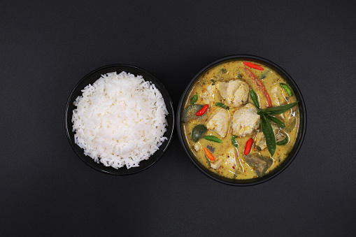 Thai food. Chicken green curry with rice in black bowl isolated on dark black background. Ingredients Green curry chicken, coconut milk, curry paste, basil, chicken breast, kaffir lime leaves, garden paprika, top view.