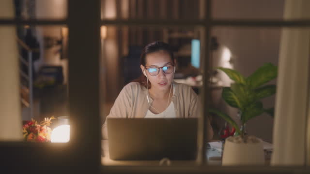 Mujer que tiene una videollamada mientras usa una computadora portátil que trabaja por la noche photo