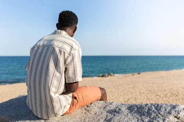 istock Back view of black man relaxing looking at the ocean. Copy space. 1397494305