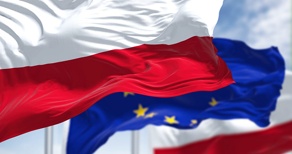 Detail of the national flag of Poland waving in the wind with blurred european union flag in the background on a clear day. Democracy and politics. European country. Selective focus.