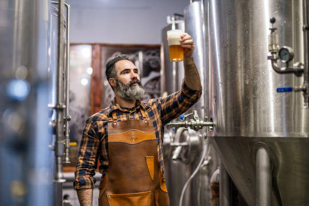 Craft beer production Bearded brewery master holding glass of beer and evaluating its visual characteristics. Small family business, production of craft beer. microbrewery stock pictures, royalty-free photos & images