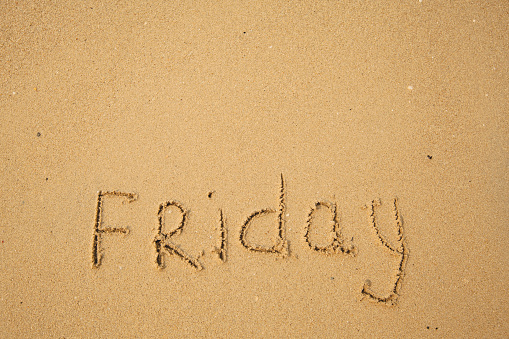 Friday - drawing of days of the week, handwritten on the sea beach sand.
