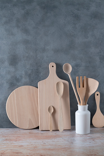 Modern kitchen kitchenware in light wood color with ladle, cutting boards and cookware on contemporary gray cement wall