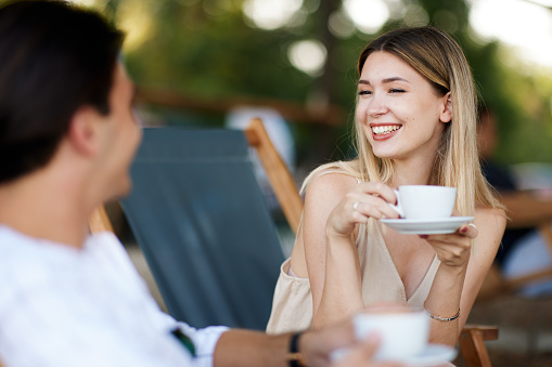 Young woman and a man enjoy coffee and chat in a summer cafe