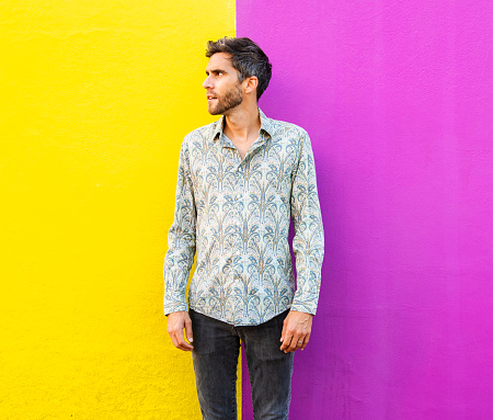 Stylish young man with a beard wearing a paisley shirt standing in front of a bright pink background