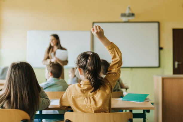 school girl in classroom putting up hand stock photo