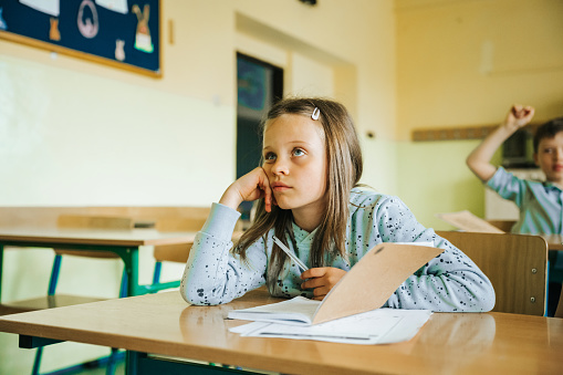 portrait of pensive elementary schoolgirl sitting head in hands and listening to lesson