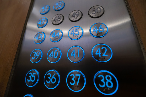 Close-up of blue glowing elevator buttons with Braille characters, numbers from the 35th floor to the 52nd floor