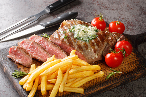 Freshly grilled steak with French Fries, green butter and tomatoes closeup on the wooden board on the table. Horizontal