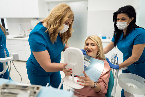 Caucasian female dentist with a female patient choosing the right teeth color for teeth whitening