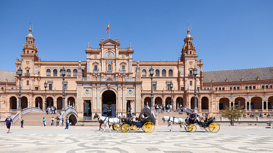 Seville, Spain - 7th April 2022. Visitors and locals enjoying a sunny April day at the Plaza de España. Some are walking while others are taking a horse-drawn carriage ride. The Plaza de España was designed by Anibal Gonzalez and completed in 1929  as the Pabellon de Andalucia for Expo 29.