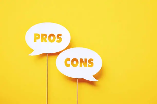 Pros and cons written circular white chat bubble sitting on yellow background. Horizontal composition with copy space.