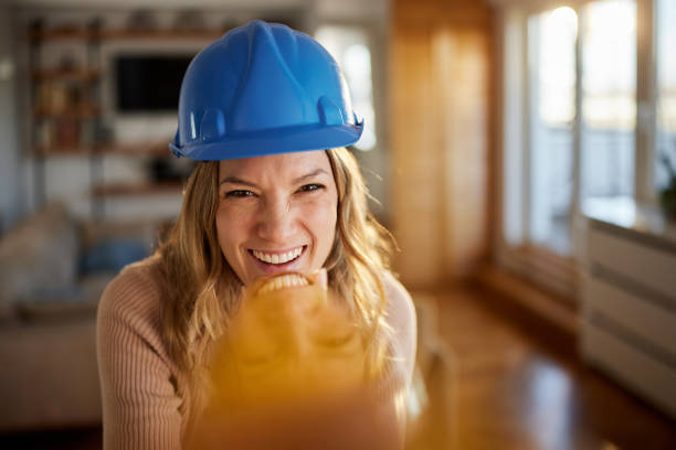 Happy female building contractor having fun while making a reflection on her face with cell phone and looking at camera.