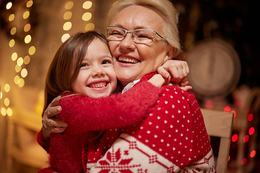 Happy mature woman embracing her small granddaughter at home on Christmas day.