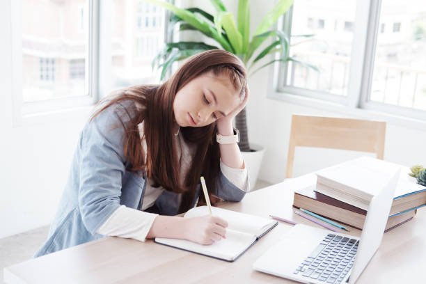 istock Serious Caucasian girl student is writing on notebook. She so bored about online learning and doing many homework with laptop at home. Education and technology for homeschool concept. 1397513247