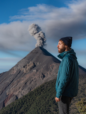 Young Caucasian man standing on the background of eruption of Fuego volcano in Guatemala