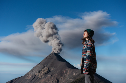 Young Caucasian woman standing on the background of eruption of Fuego volcano in Guatemala