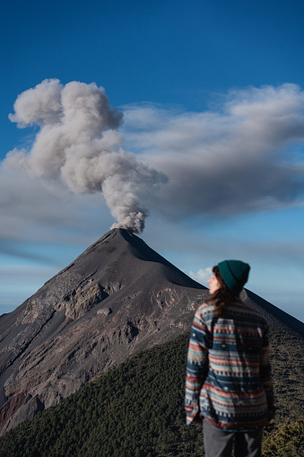 Young Caucasian woman standing on the background of eruption of Fuego volcano in Guatemala