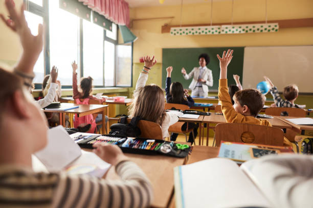 istock Back view of students raising their hands to answer the teacher's question on a class. 1397515933