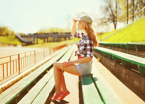 Portrait of beautiful young blonde woman wearing baseball cap, shorts and shirt in summer park