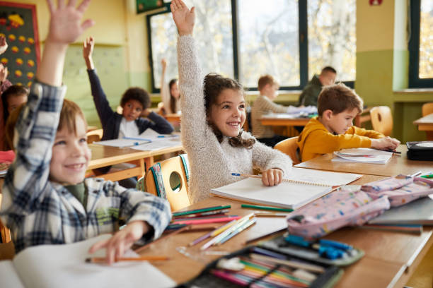 istock Happy elementary students raising their hands on a class at school. 1397516878