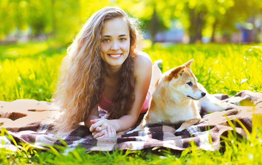 Summer portrait of happy smiling girl with dog on green grass in city park