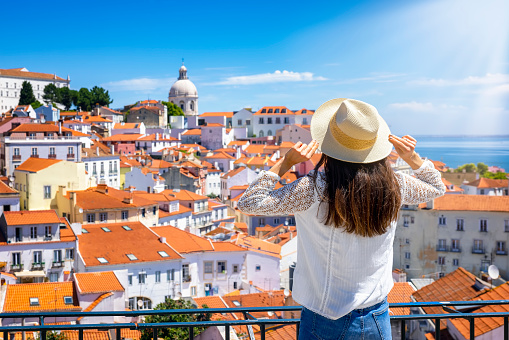 A tourist woman looks at the beautiful cityscape of Lisbon, with the colorful houses and roofs at the Alfama district, Portugal
