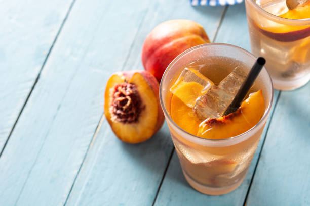 Glass of peach tea with ice cubes on blue wooden table