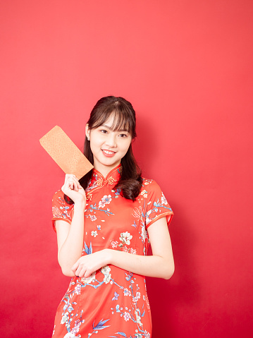 Portrait beautiful young asian woman wearing traditional cheongsam qipao dress with red envelopes in chinese new year concept on red background.