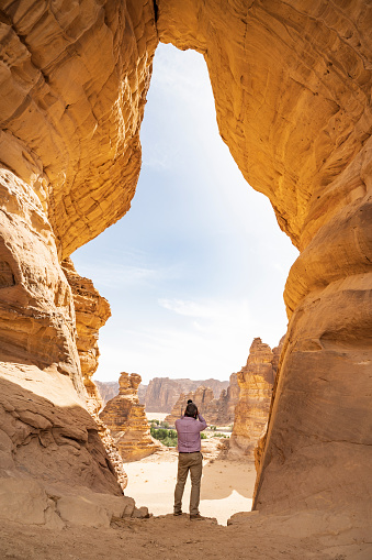 Full length rear view of professional landscape photographer standing within eroded opening looking out on Elephant Rock and other natural formations.
