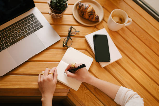 istock Young woman freelancer working online using her laptop, sitting in a coffee house and drinking coffee. Top view. 1397526716
