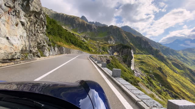 Passenger vehicle driving on a majestic empty winding mountain road overlooking waterfall and lush green valley