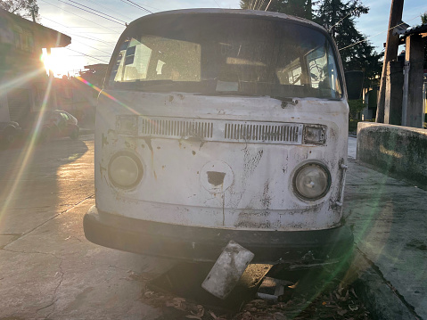 An old white van of a classic model that was popular in the 1960s and 1970s, parked, abandoned and missing parts