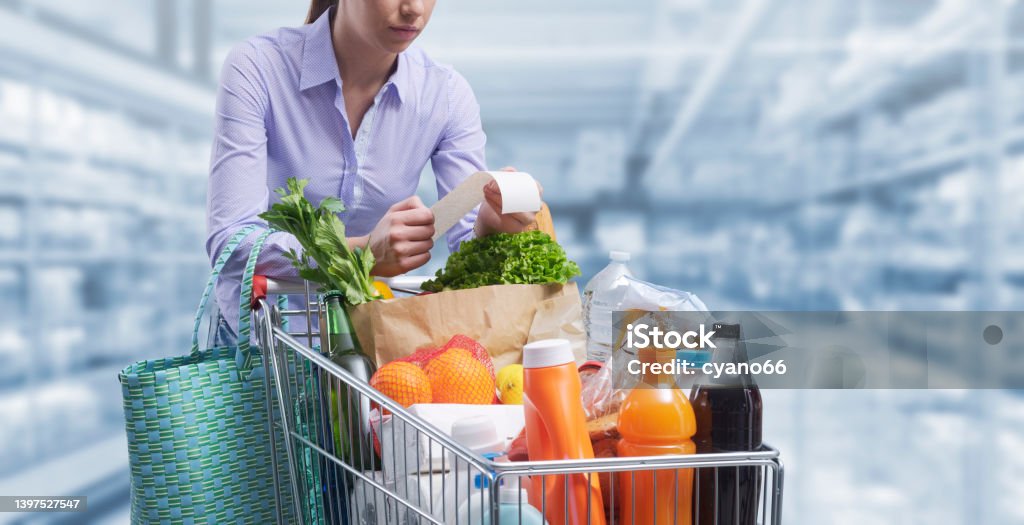 Woman checking a grocery receipt at the supermarket Woman pushing a cart and checking a grocery receipt, grocery shopping and expenses concept Supermarket Stock Photo