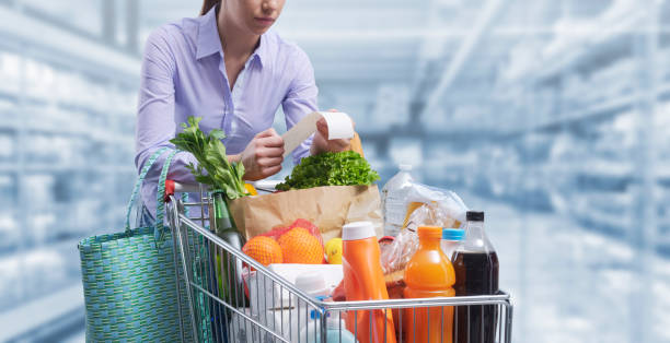 Woman checking a grocery receipt at the supermarket Woman pushing a cart and checking a grocery receipt, grocery shopping and expenses concept receipt stock pictures, royalty-free photos & images