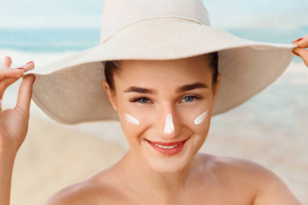 Beauty Woman smile applying sun cream  on face. Skincare. Body Sun protection. sunscreen. Female in hat smear  moisturizing lotion on skin. stock photo
