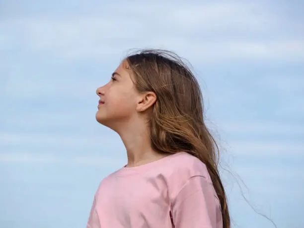 Photo of Side view portrait of a relaxed girl breathing fresh air under a blue sky on the sea in summer. Close-up side view of a beautiful teenage girl looking at the sky. freedom and traveling concept
