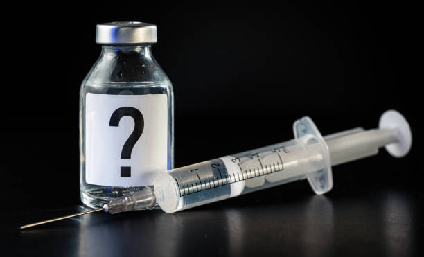 istock Vaccine bottle with hypodermic syringe needle near, question mark on label, black background - unknown side effects of experimental treatment concept 1397544101