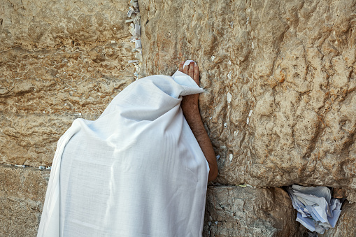 Man covered in white tallit praying at the Wailing Wall in Jerusalem, Israel.