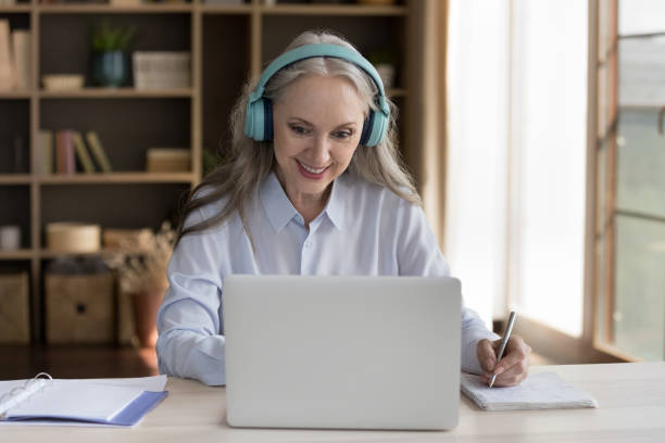 felice corso di formazione maturo studente donna in auricolari wireless - mature student learning training computer foto e immagini stock