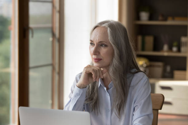istock Pensive dreamy older 60s business lady sitting at laptop computer 1397545140