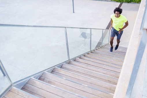 From above of fit African American male runner jogging up staircase during cardio training in city in summer