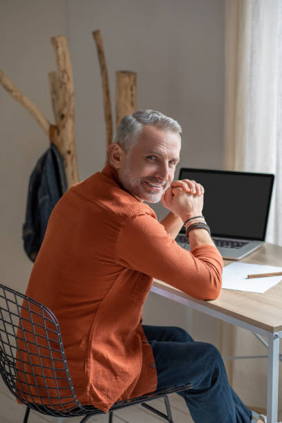 istock A man in orange shirt sitting at the table and looking contented 1397546836