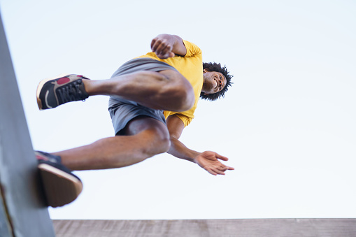 View from below of black man jumping on his run. Young male exercising in urban background.