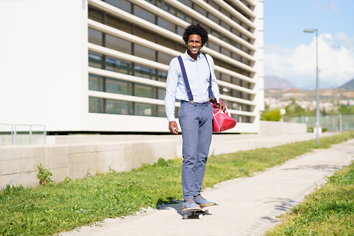 Black businessman riding skateboard near office building. Guy with afro hair.