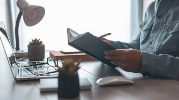 istock casual business man using mobile smart phone and laptop computer, writing on notepad on table at home office, man taking note on reminder planner 1397548269