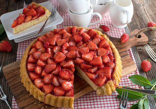 Homemade baked traditional german strawberry pie or strawberry tart. Served on rustic and wooden kitchen table with cross section view