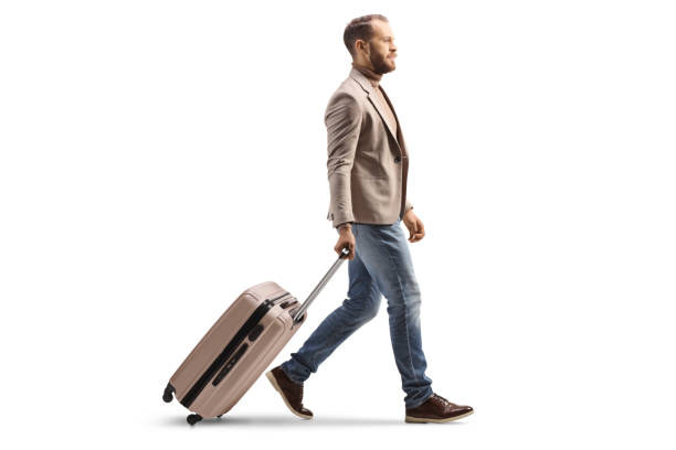 Full length profile shot of a man walking and pulling a suitcase stock photo