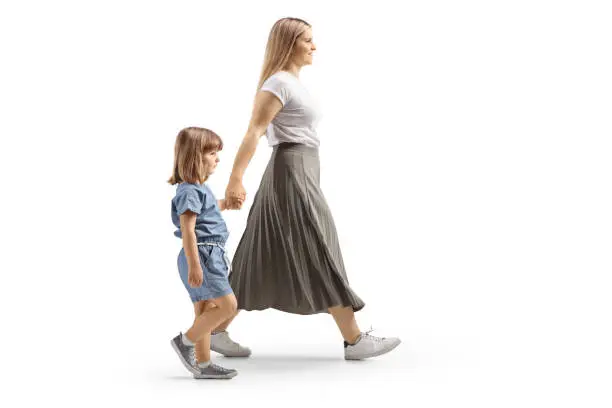 Full length profile shot of a mother and daughter walking and holding hands isolated on white background