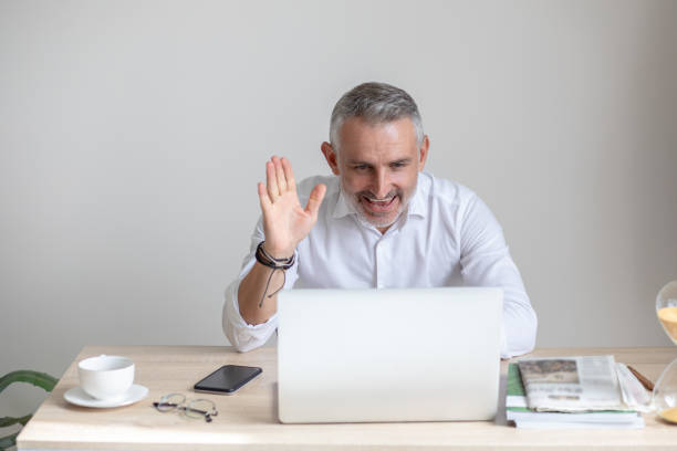 istock Man looking at laptop raising his hand in greeting 1397549823